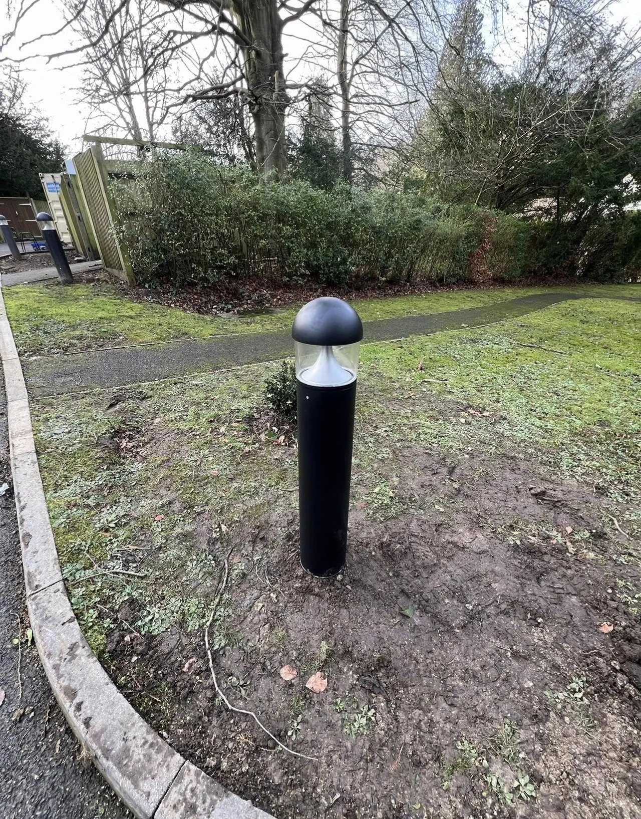 Black bollard light beside a landscaped outdoor pathway